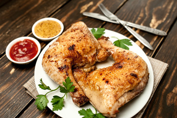 Chicken legs in a plate with mustard and ketchup on a wooden background.