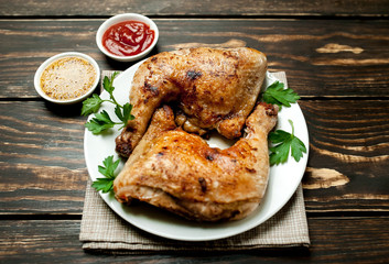 Chicken legs in a plate with mustard and ketchup on a wooden background.