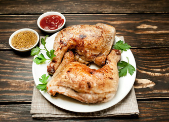 Chicken legs in a plate with mustard and ketchup on a wooden background.