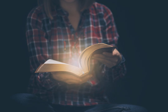 Young woman readin bible in a dark room