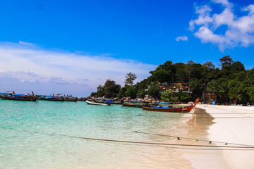 Travel Thailand. Idyllic Exotic Thai beach with turquoise water, palm trees and long tail boats - favourite tourist attraction. Popular tourist holiday/vacation destination. Bright colours. 