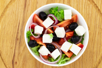Greek salad with fresh vegetables, feta cheese and black olives on a wooden background. Top view
