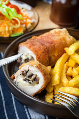 Fried chicken breast stuffed with mushrooms and cheese wrapped in ham served with fries and salad.