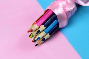 A group of colored pencils tied with a pink ribbon as a gift to the child for drawing on pink and blue background