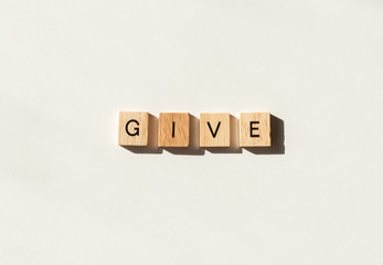 The word GIVE spelled in wooden letter tiles flat lay on white.