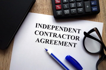 Independent contractor agreement, pen, glasses and   calculator on desk