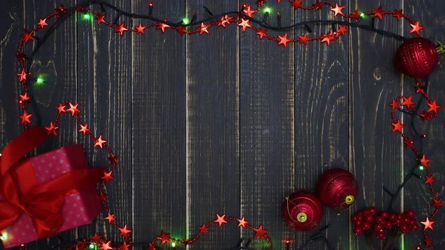 Beautiful defocused Christmas flatlay footage background. Top view of blurry holiday colourful lights of led lamp garland, red ornaments and small present gift box in wrapping paper with bow.