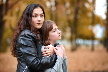 Pretty woman and teen girl are posing in autumn park. Beautiful landscape at fall season.