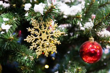 New year toys, red sphere and golden snowflake on snowy branches of christmas tree