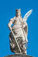 Statue of Catherine with writing bird feather, sword and cartwheel at ancient portal in Magdeburg, Germany, closeup, blue sky