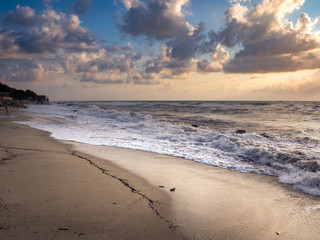 Beach at sunset with choppy sea and waves crashing to shore.