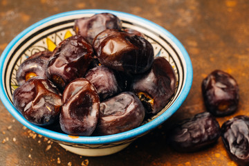 Dried dates in an oriental ceramic bowl on a dark background. Ramadan snacks