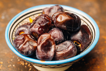 Dried dates in an oriental ceramic bowl on a dark background. Ramadan snacks