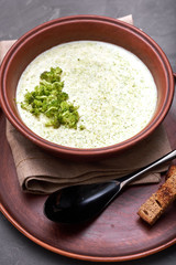 Delicious broccoli cream soup in a beautiful clay bowl. Soup-puree and small toasts of rye bread. Exquisite black dining spoon and a napkin of coarse cloth. Gourmet restaurant lunch.