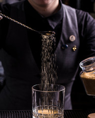 Bartender making refreshing coctail on a bar background. Dark moody style. Ice in tha glass