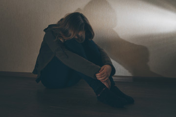 Sad teenage girl sitting near laptop in dark room. She is a victim of online bullying Stalker...