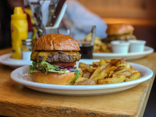 Tasty grilled beef burger with lettuce and mayonnaise served on brown paper on a wooden table. French fries. Copy space. Selective focus.