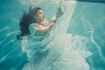 sexy young bride swimming underwater in white wedding dress, stockings and gloves