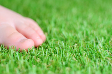 Artificial grass. Tender baby foot on a green artificial turf floor.