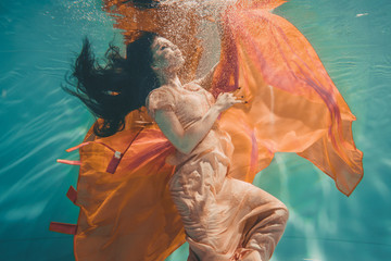 girl with orange dress is dreamy and meditative floating under water, like the soul before...