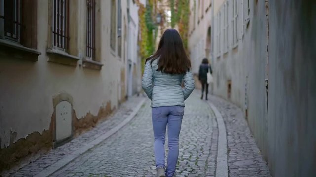Outside shot from behinf of a lovely brunnete walking on very narrow street.