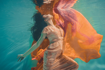 girl with orange dress is dreamy and meditative floating under water, like the soul before reincarnation