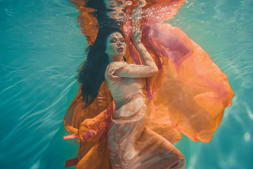 girl with orange dress is dreamy and meditative floating under water, like the soul before reincarnation