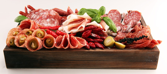 Food tray with delicious salami, pieces of sliced prosciutto crudo, sausage and basil. Meat platter with selection
