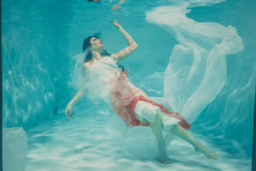 beautiful model girl swimming underwater in feminine long white and pink dress