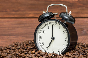Alarm clock and coffee beans on a wooden background. Alarm clock standing on the beans of coffee....