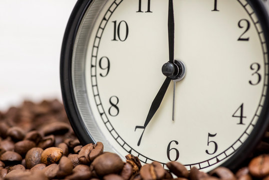 Alarm clock and coffee beans on white wooden background. Alarm clock standing on the beans of coffee. Coffee time concept