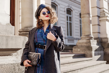 Outdoor fashion portrait of young beautiful fashionable girl wearing blue checkered dress, grey...