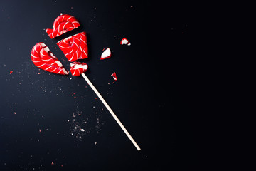 Broken lollipop in shape of heart on a dark background with copy space