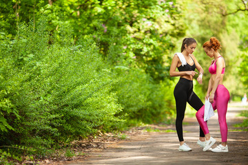Fitness. Two female runners stretching legs outdoors in park in summer