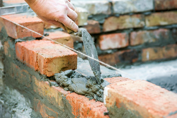 Bricklayer worker installing brick masonry on exterior wall. Professional construction worker laying bricks. Bricklayer worker installing bricks on construction site
