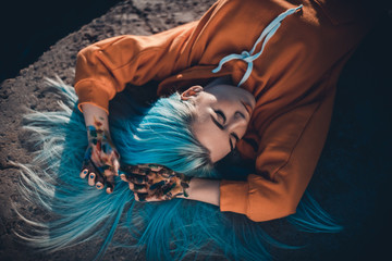 Portrait of young artist woman in orange sweatshirt with blue hair 