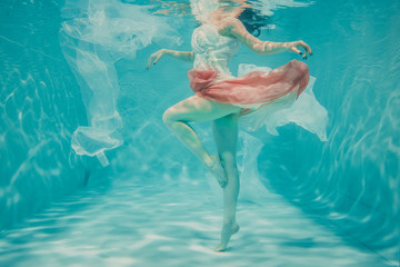 beautiful model girl swimming underwater in feminine long white and pink dress