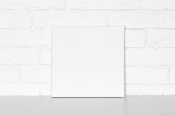 Blank square canvas in interior. Brick wall on background.
