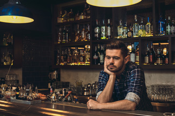 Young bartender leaning on bar counter thoughtful