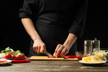 The chef cuts hot chilli peppers. For the preparation of pizza, salad. A delicious and spicy food concept, Mexican, cooking. On a black background for design or lettering text.