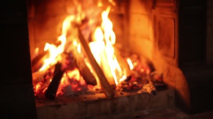 Young stylish man in knitted sweater throwing wooden logs in fireplace at home. Unrecognizable caucasian male puts wood in the stove hearth in wooden cottage. Guy drowns a fire in his house. - Powered by Adobe