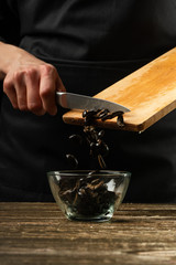 The chef pours olives. Frosting in motion. For cooking pizza, salad. A delicious meal concept. On a black background for design or lettering text.
