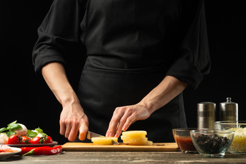 The chef cuts the pineapple. For the preparation of pizza, salad. The concept of delicious food and healthy food. On a black background for design or lettering text. Close-up