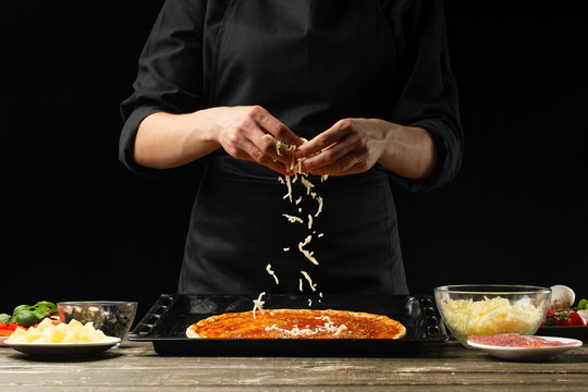 The chef sprinkles pizza with mazzarella cheese. The concept of delicious food and healthy food. On a black background for design or lettering text.