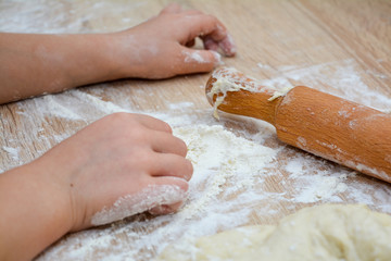 Cooking baking at home - children's hands, rolling pin, flour and dough. The child is preparing a cake.