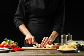 The chef cuts champignon mushrooms with vegetables. For the preparation of pizza, mushroom sauce, salad. A delicious food concept, cooking. On a black background for design or lettering text