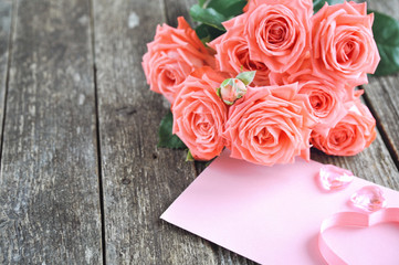 Delicate coral shade pink roses and gift with heart and letterhead on rustic wooden background....