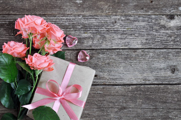 Delicate coral shade pink roses and gift with heart and letterhead on rustic wooden background....