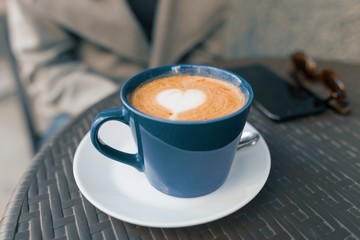 Coffee art with a heart in blue cup on table in an outdoor cafe