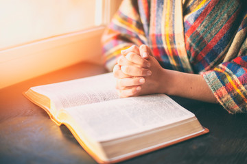 Woman with praying over her opened bible in the sunlight